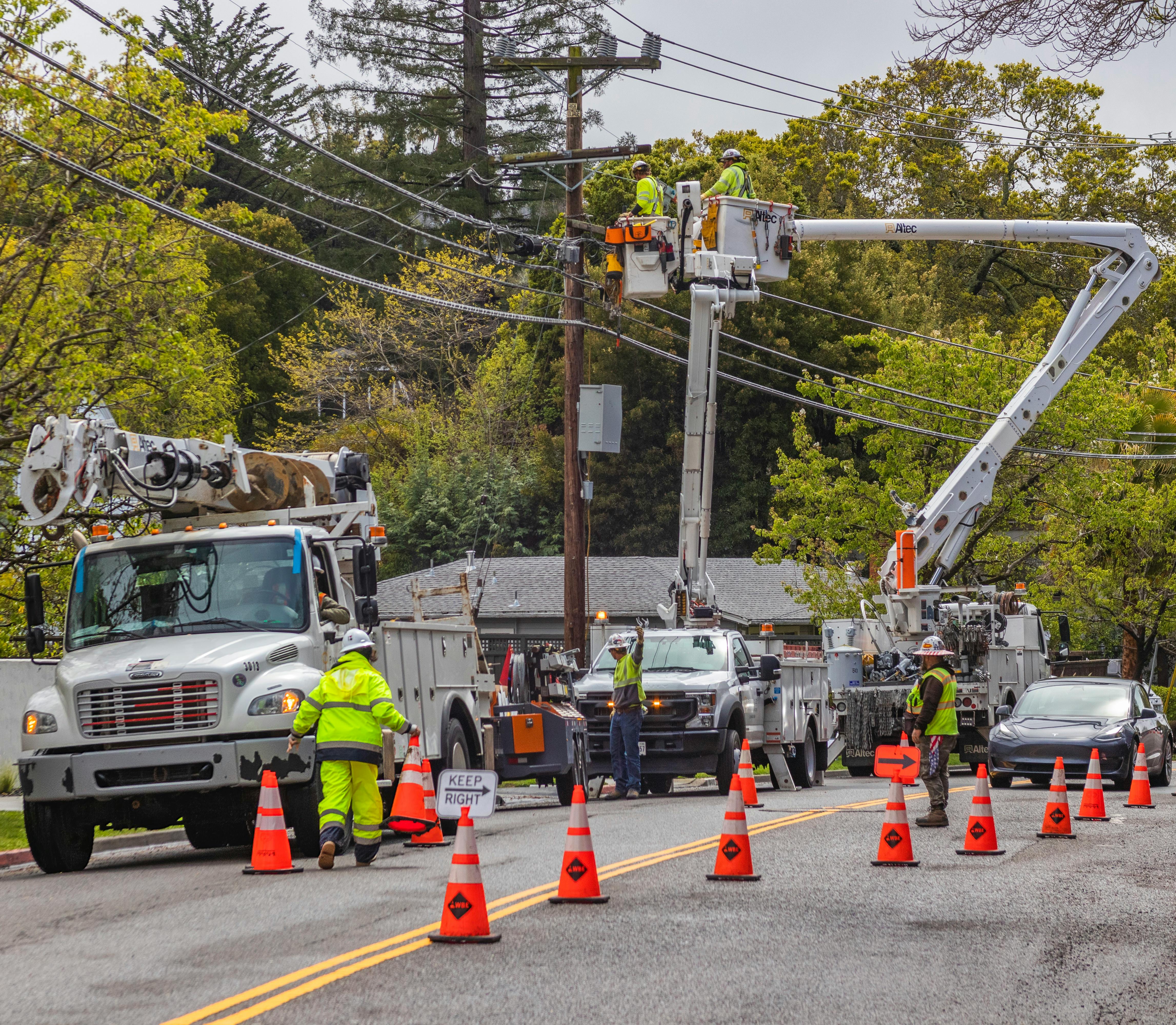 Utility workers in a bucket truck by electrical wires surrounded by orange cones